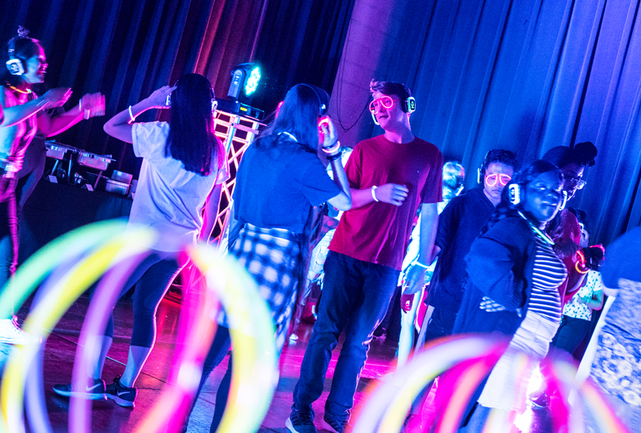 Students dancing with head phones on and neon colors surrounding them